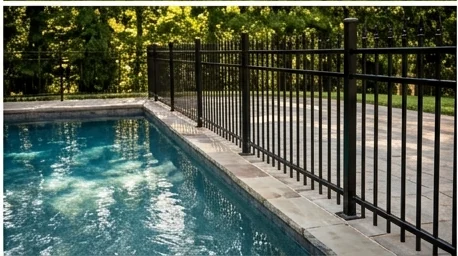 Black ornamental aluminum pool fence with flat-top pickets beside a pool deck